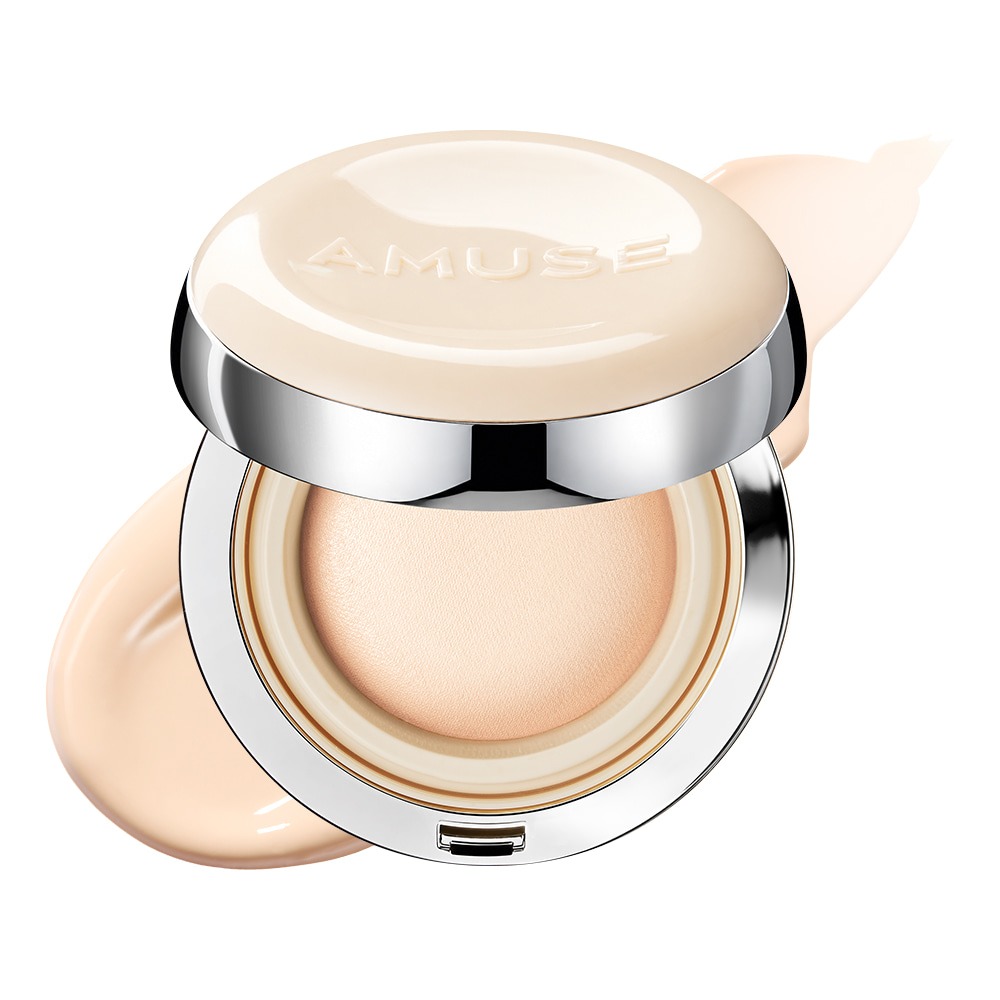 Open AMUSE cushion compact with a cream glossy lid and silver rim, showing a pale beige domed balm, with a smear of light foundation behind it.