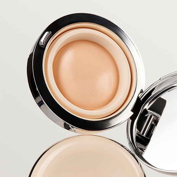 Close-up of an open compact showing a smooth, domed beige balm cushion inside a silver rim.