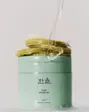 A sage-green Hanyul jar topped with a stack of green pads, with clear essence pouring onto them