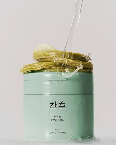 A sage-green Hanyul jar topped with a stack of green pads, with clear essence pouring onto them