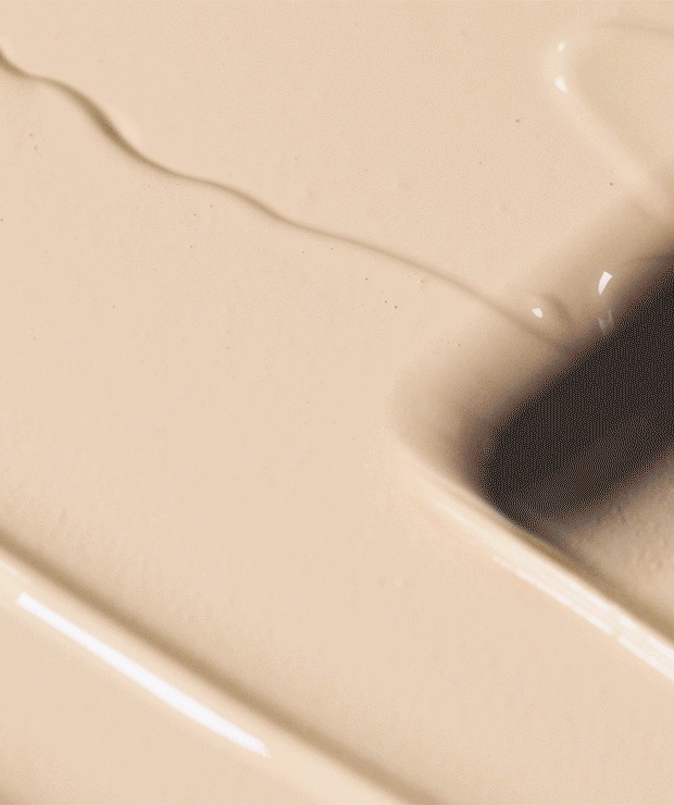 Close-up of glossy, light beige liquid foundation spread in a smooth layer with a ridge where a puff has pressed it.