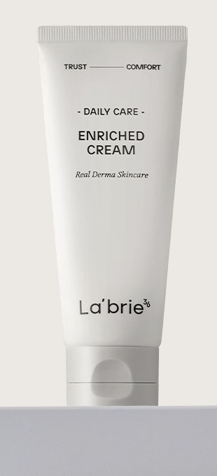明るいグレーの背景で、白い台の上にキャップを下にして立つ、La'brie「Daily Care Enriched Cream」のライトグレーのチューブ。