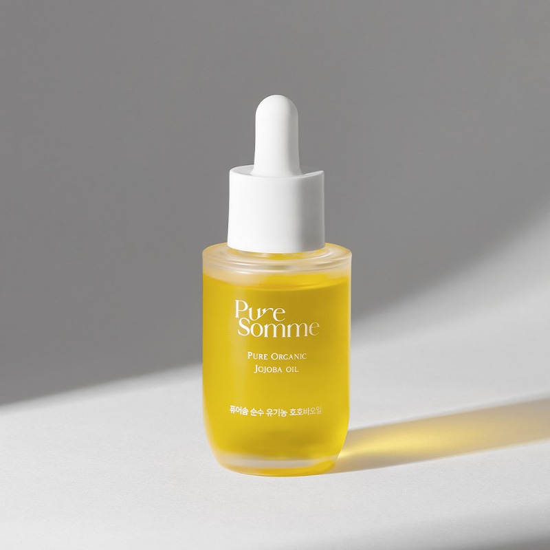 グレーと白の背景にやわらかな横光を受ける、黄金色のオイルが入ったPure Somme「Pure Organic Jojoba Oil」30mlのすりガラス調スポイトボトル。キャップは白。