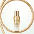 A gold REJURAN Healer pump bottle standing inside a curved gold ring on a pale background