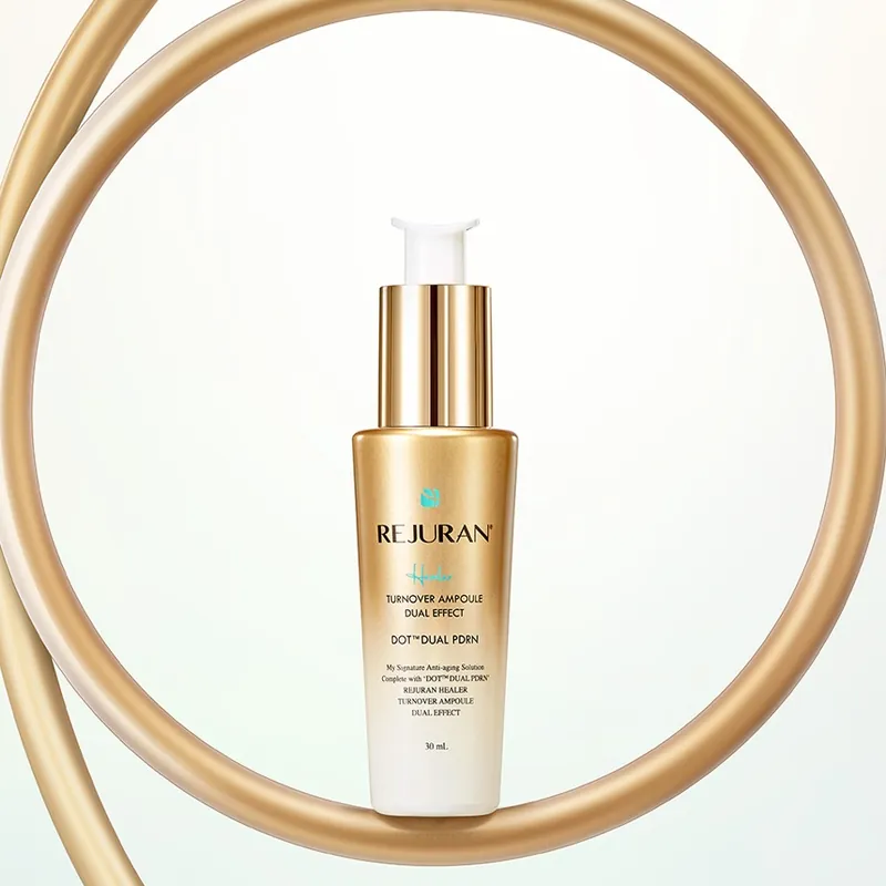 A gold REJURAN Healer pump bottle standing inside a curved gold ring on a pale background