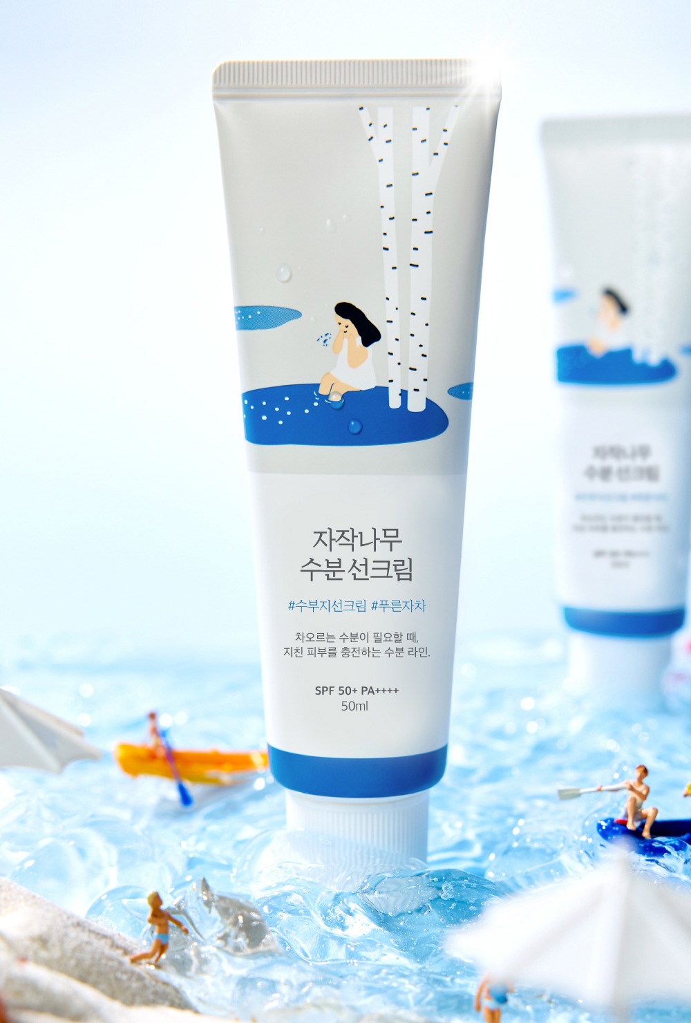 韓國版 Round Lab 樺樹保濕防曬白色軟管（韓文標籤、SPF 50+ PA++++、50ml）立在清水中，周圍有迷你海灘人偶。