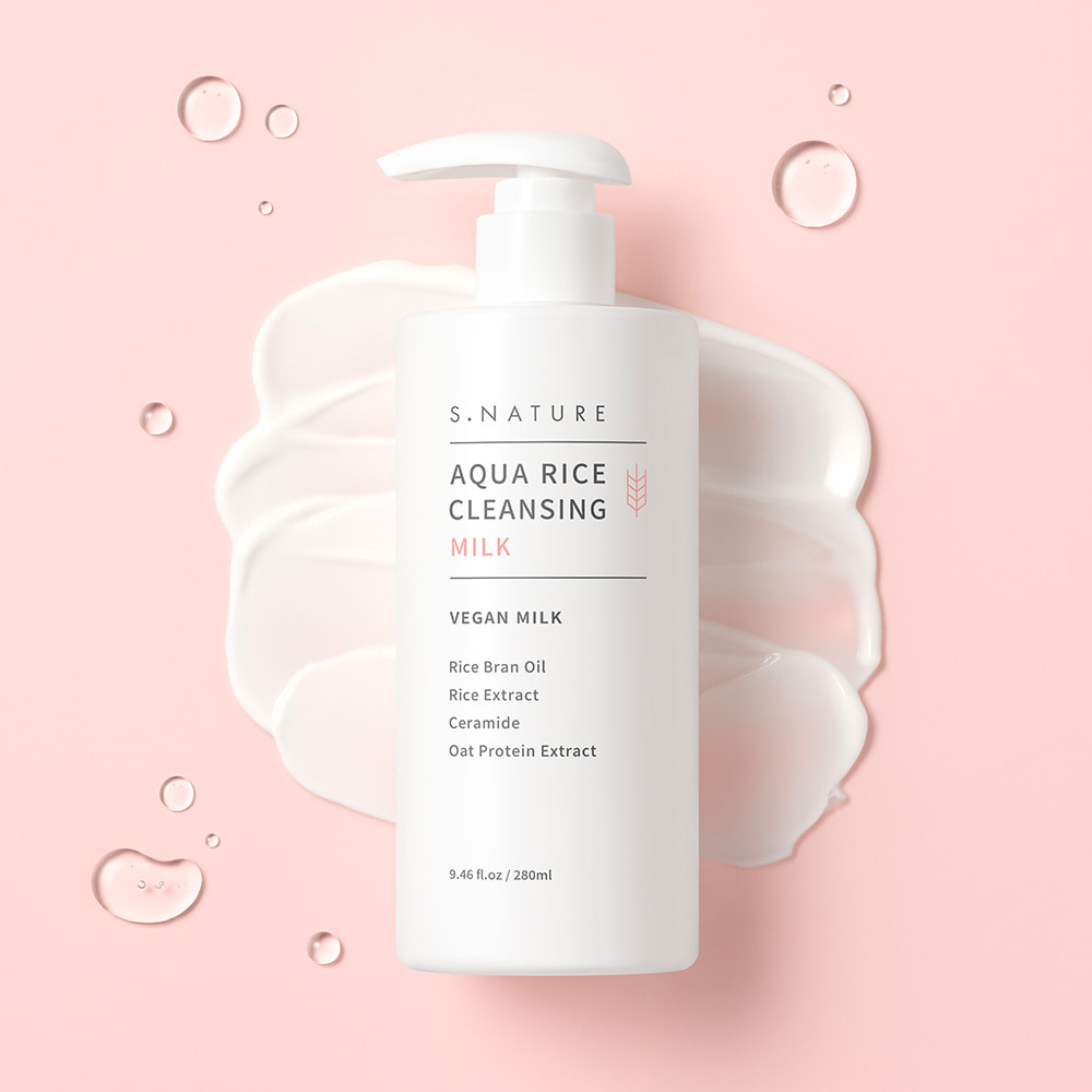 El frasco blanco de 280 ml con dosificador, tumbado sobre una superficie rosa pálido encima de una amplia pincelada espesa de leche limpiadora blanca, con gotas de agua transparentes alrededor.